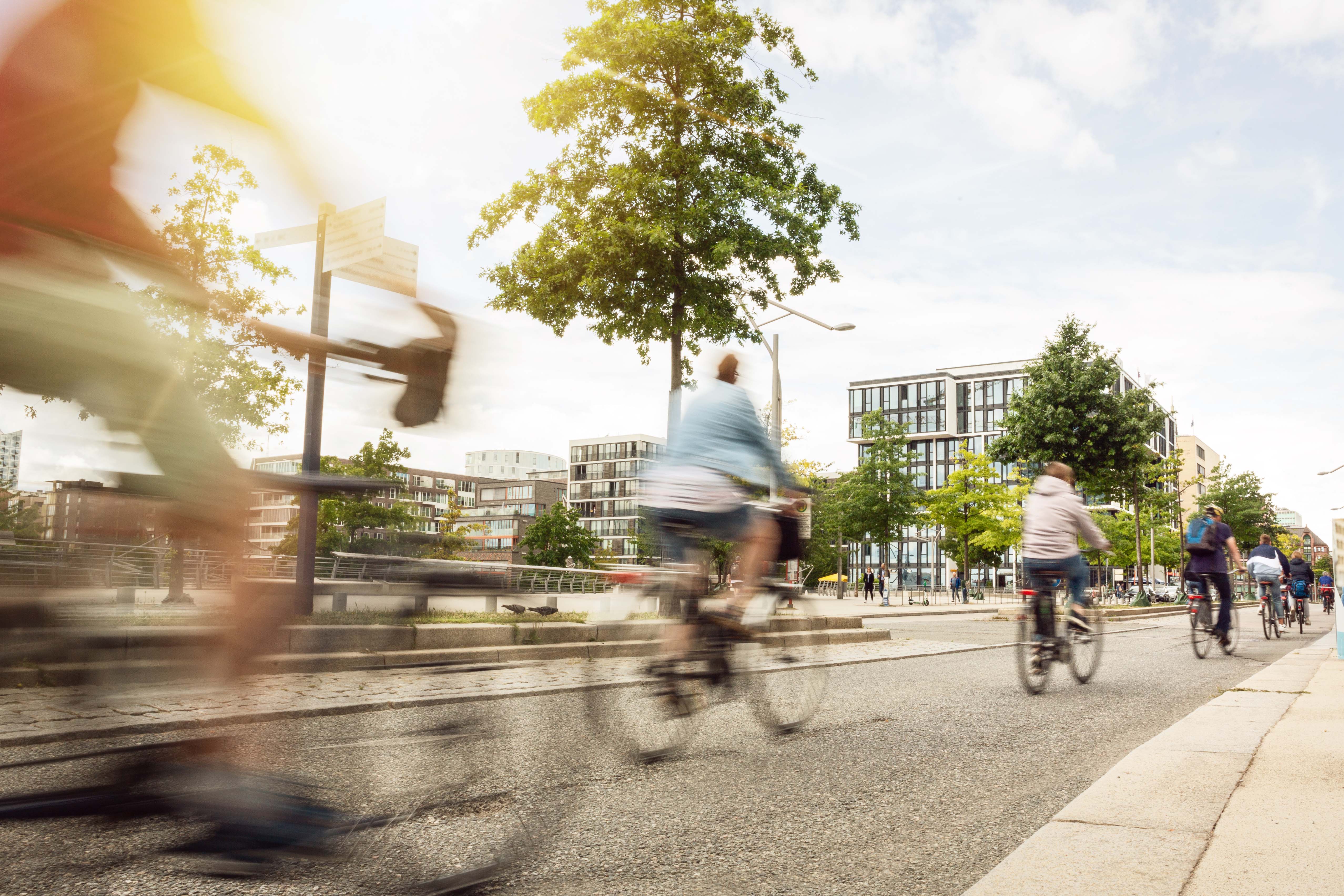 Grupo de pessoas andando de bicicleta em uma área urbana moderna, com prédios residenciais ao fundo, em um dia ensolarado.