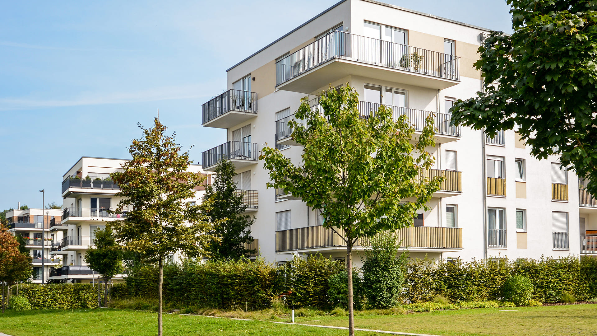 Fachada de um condomínio residencial moderno, com varandas, áreas verdes e árvores ao redor, representando o conceito de gestão sustentável e bem-estar coletivo.