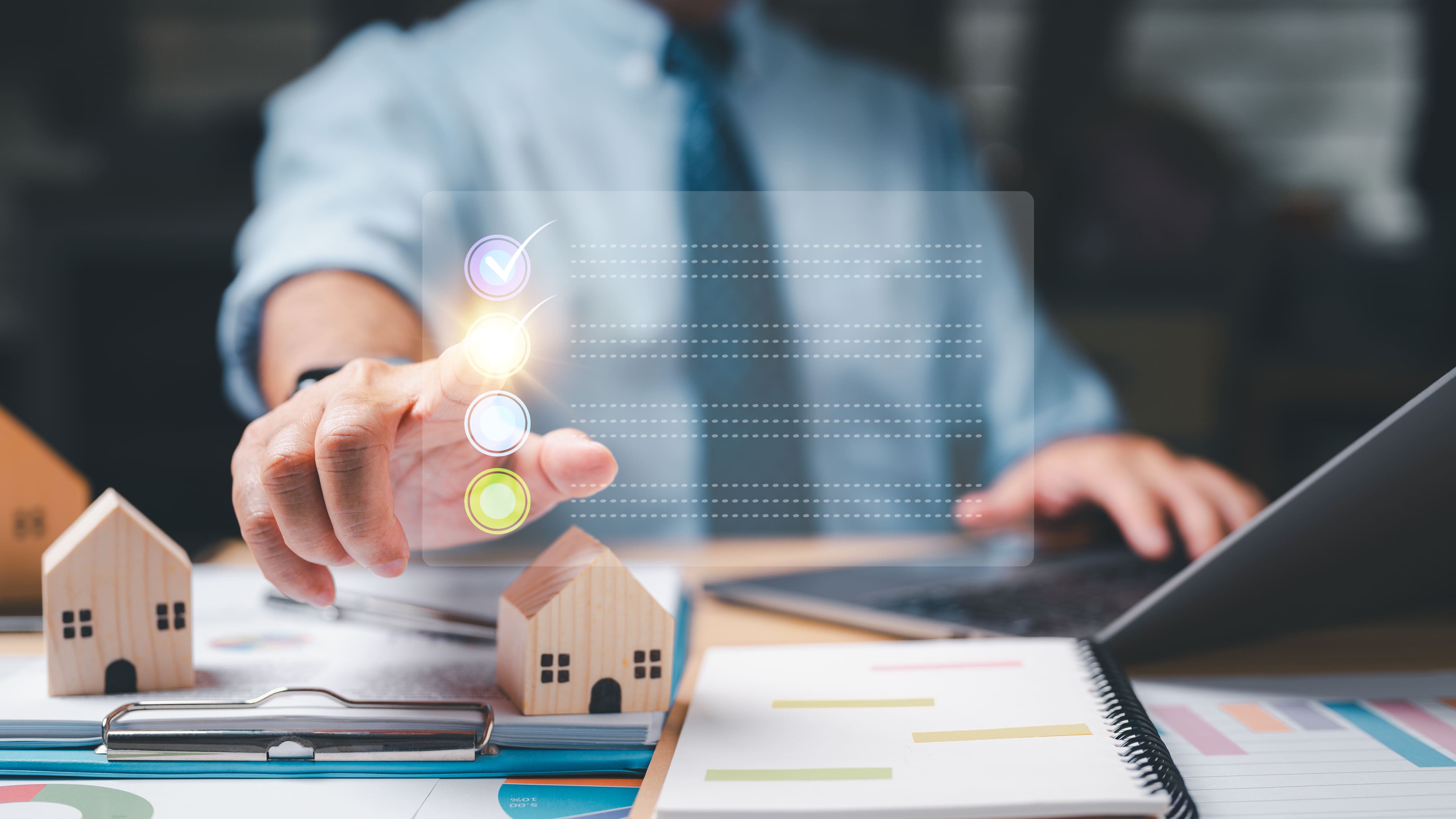 Síndico revisando checklist digital de manutenção preventiva em ambiente de trabalho, com miniaturas de casas, gráficos e laptop ao fundo. A imagem representa a importância do planejamento estratégico e da organização para garantir o bom funcionamento do condomínio, mesmo quando tudo parece estar sob controle.
