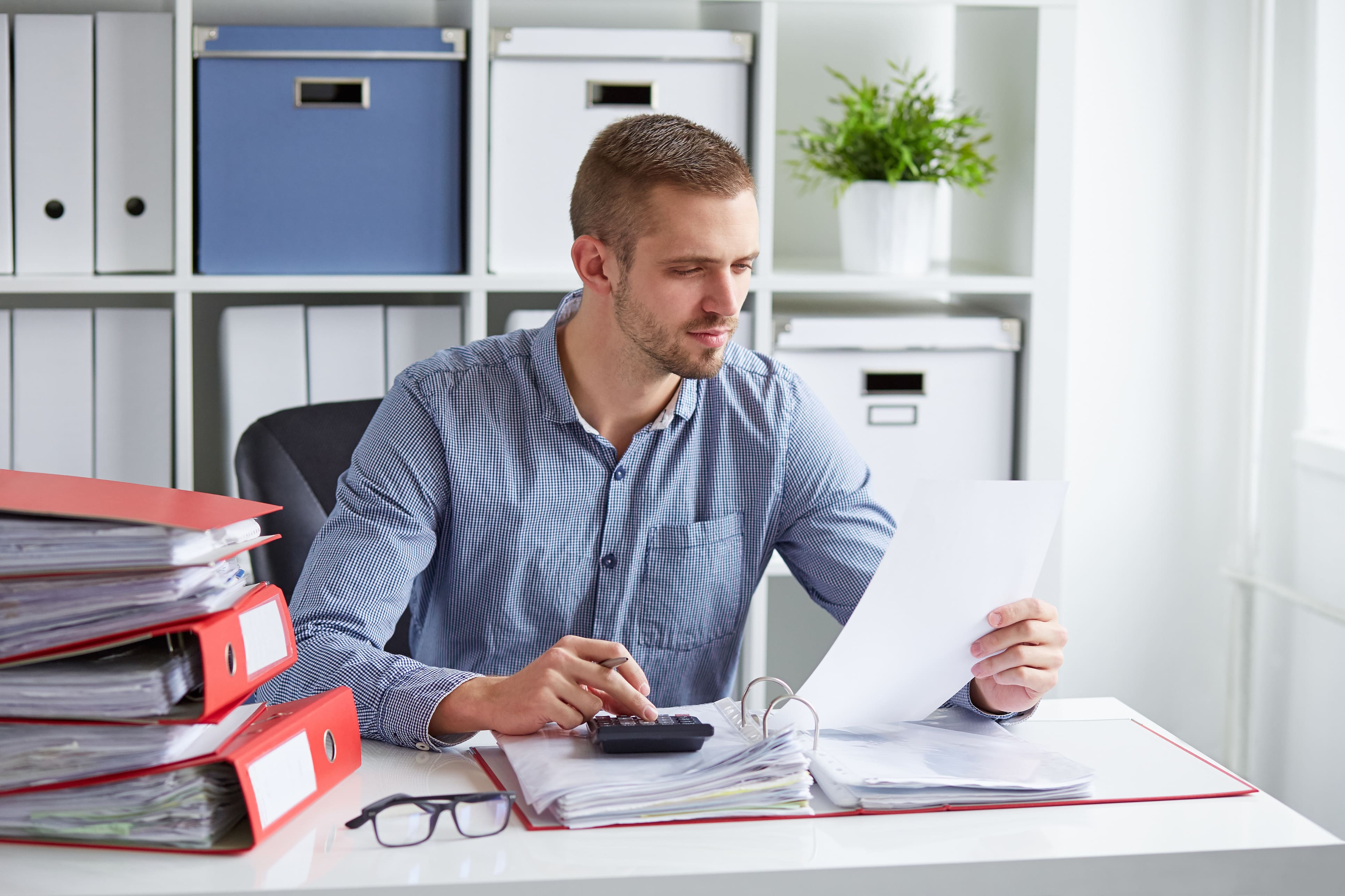 Síndico analisando documentos financeiros com calculadora e pastas organizadas sobre a mesa, representando o planejamento orçamentário na gestão condominial preventiva.
