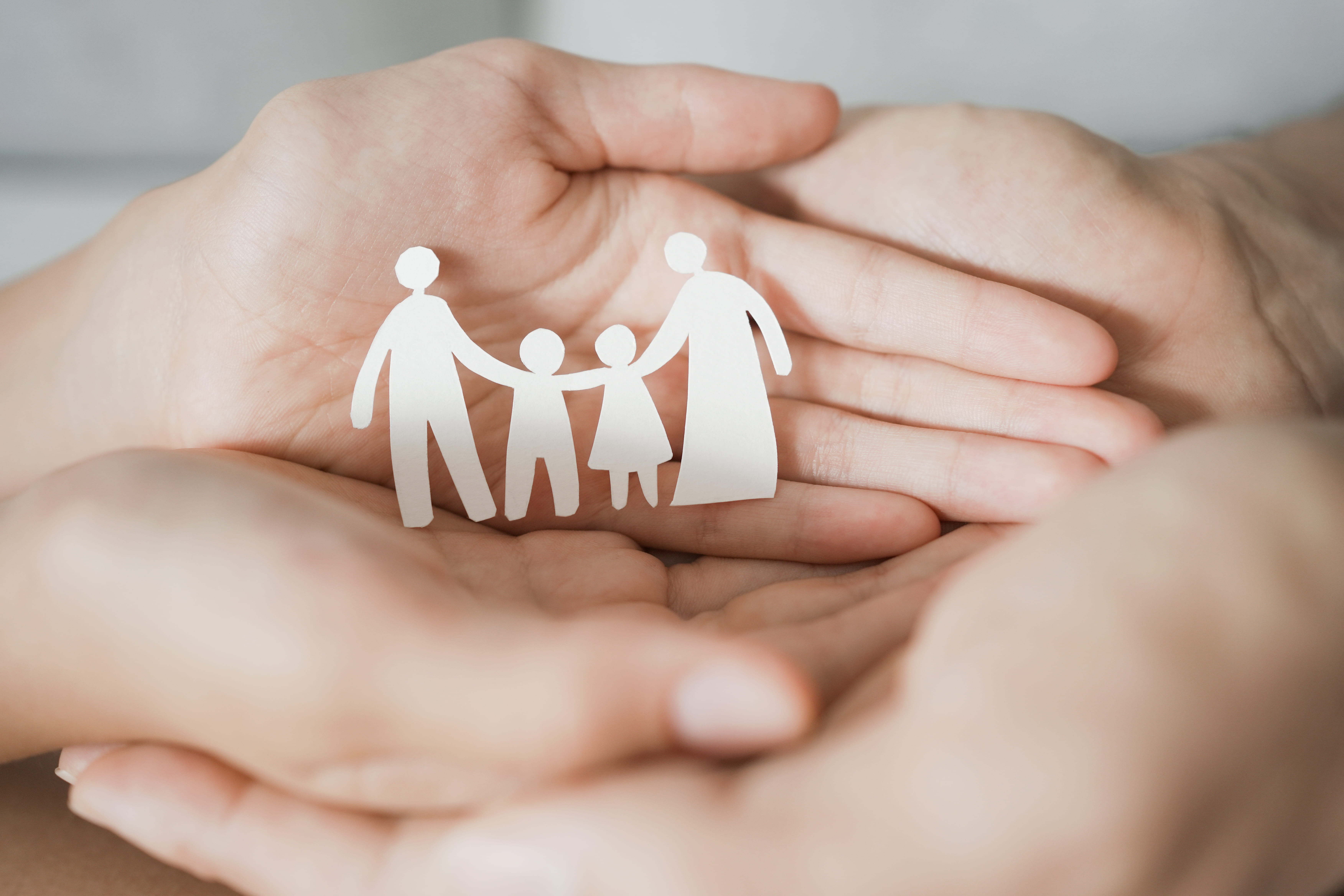 Mãos em posição de acolhimento segurando recorte de papel representando uma família, simbolizando proteção, cuidado e segurança em casos de violência doméstica.